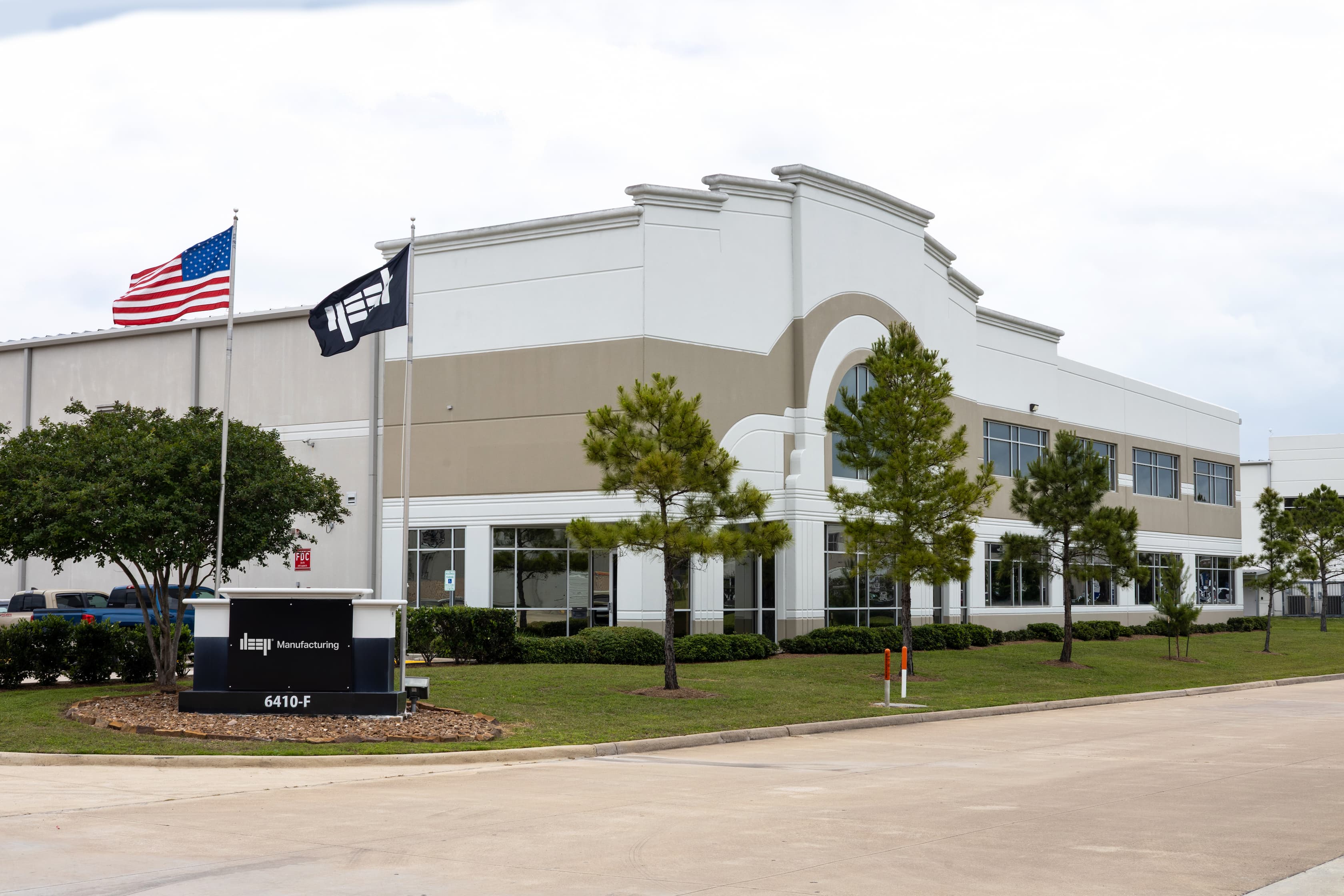 The front of a large warehouse, with a grand frontage, and American flag, a DEEP flag and a DEEP Manufacturing branded plinth. 