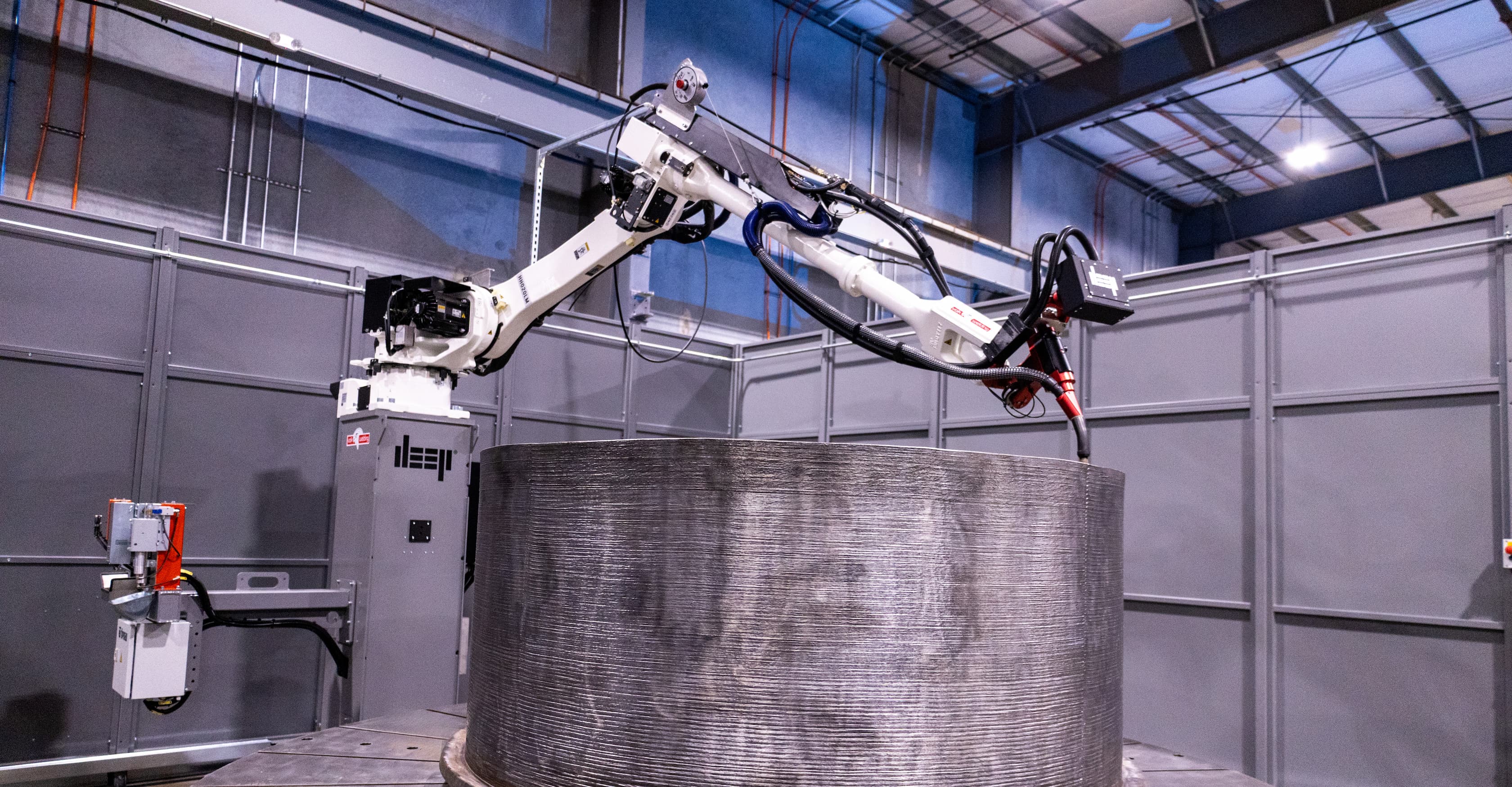 A WAAM robots over a 3D printed metal cylinder.