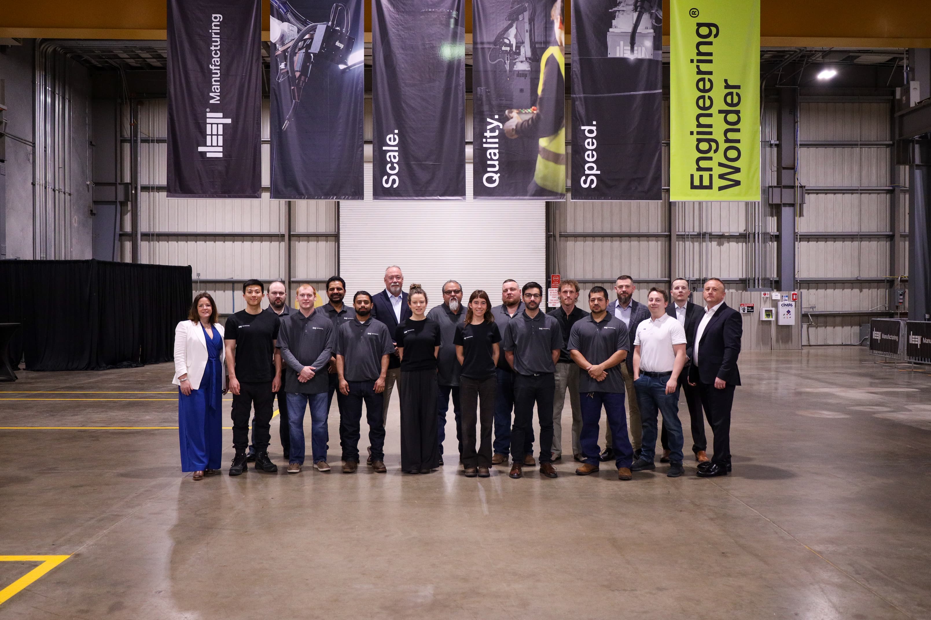 A photo of the DEEP Manufacturing team under flags reading 'Scale, Quality, Speed'