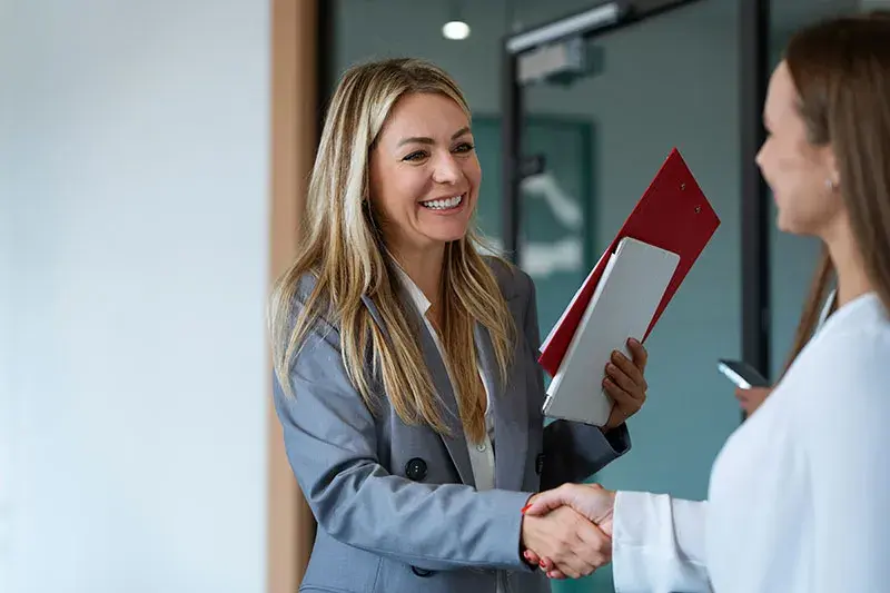 Due professioniste si stringono la mano con calore e apertura, esempio concreto di soft skill come la comunicazione e l'espansività nel mondo del lavoro.